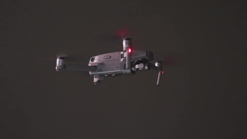 A drone white blinking lights uses rotors to float on a grey background