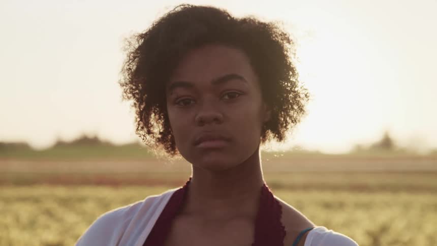 Close up of an african american woman looking at the camera on a prairie of flowers at sunset