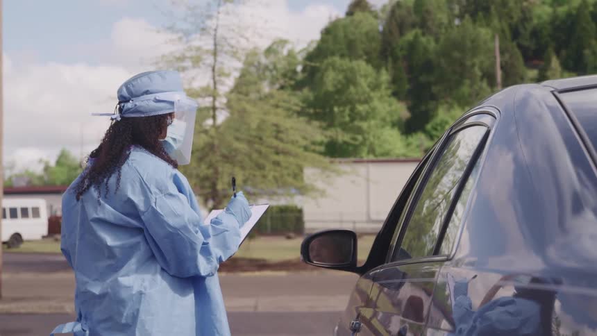 Woman wearing protective gear stops a car on a medical checkpoint