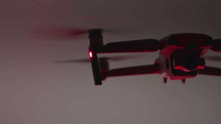 A drone with propellers hovering with the sky and clouds in the background