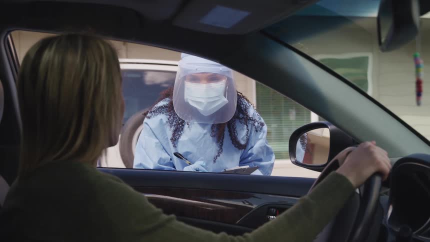 Driver talks to medical personnel wearing protective gear through window