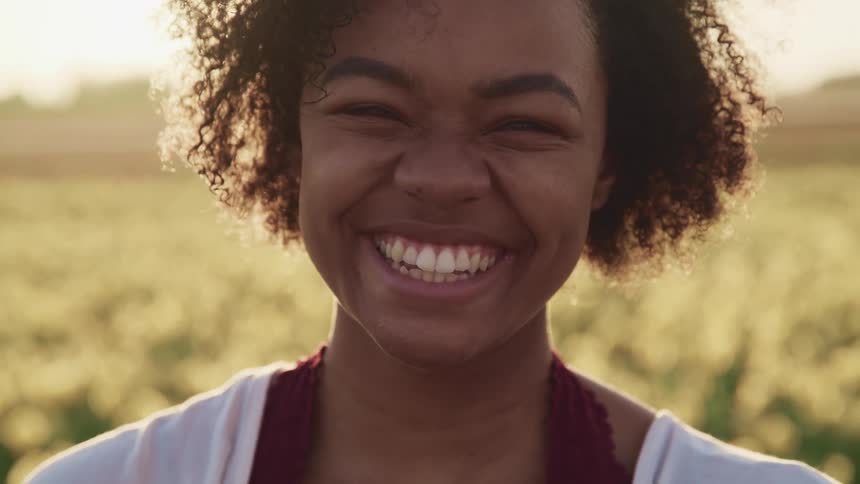 Young woman smiles at the camera while standing in front of a tulip field at sunset
