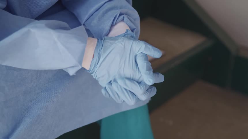 Person wearing blue latex gloves and scrubs sits in the stairs of a building