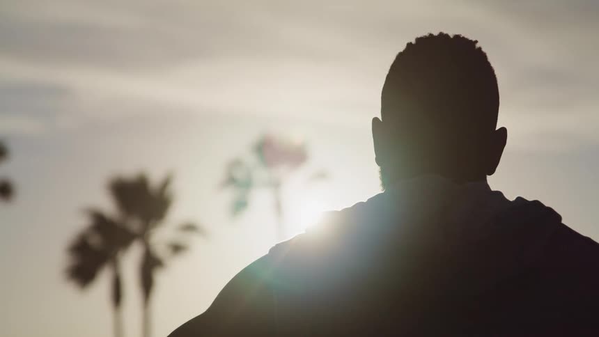 Basketball player with a beard and a hoodie is silhouetted against the sun