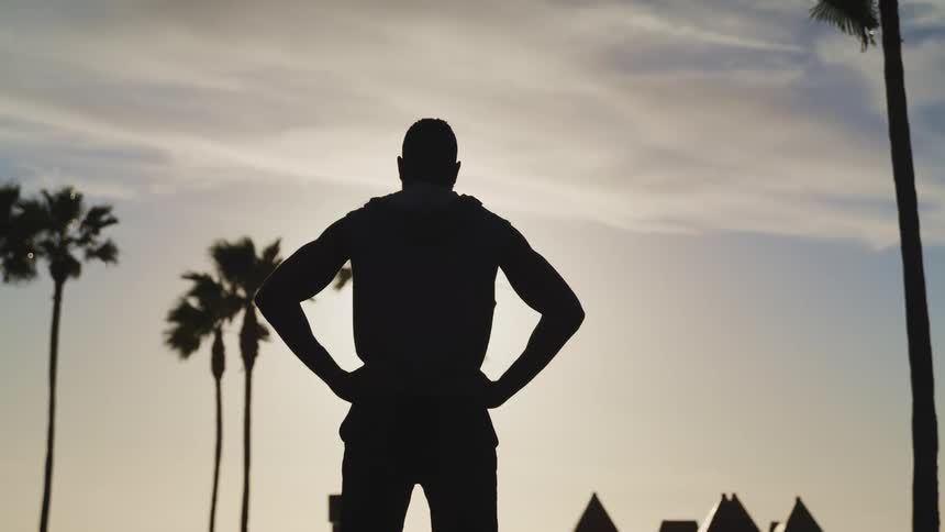 A silhouette of a man standing with trees the sky and clouds in the background