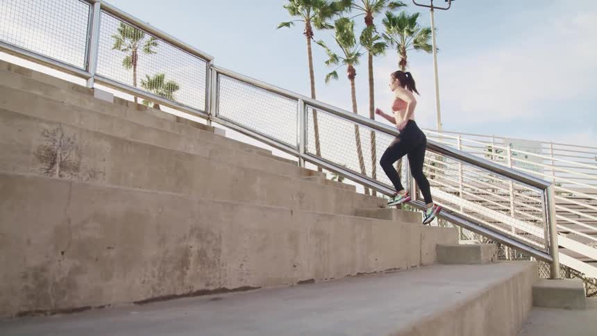 Woman working out runs up the concrete stairs on a public park