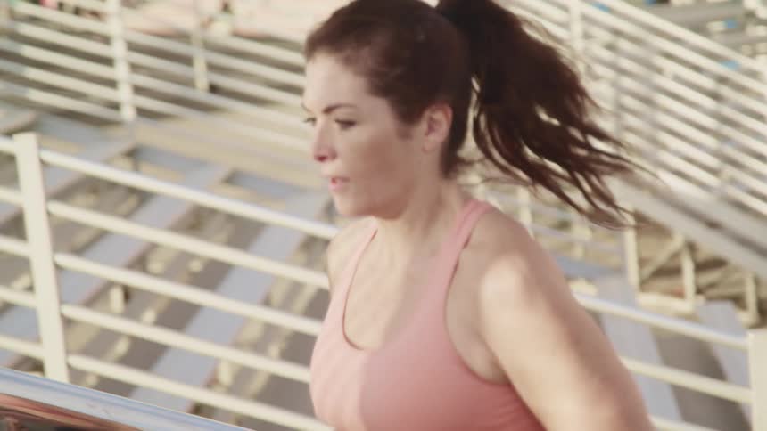 Young woman wearing sports clothing jogs up a concrete stair in a park