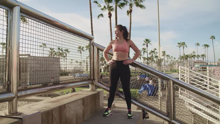 Woman in sports clothing stands on the stairs of a park at sunset