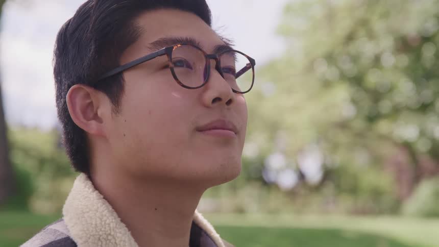 Side view of an asian man with glasses looking up and smiling slightly