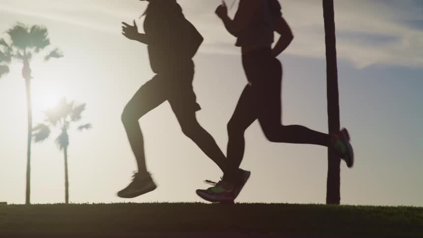 A young couple jogging together near to palm trees at sunset