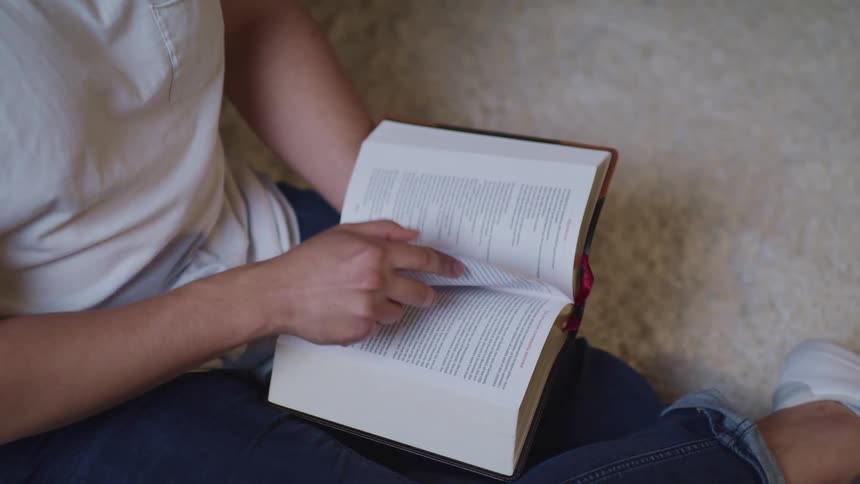 A person sitting on a white rug reading a book in a room