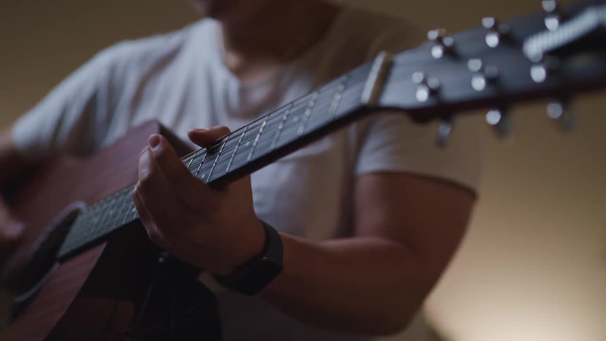A man in a white t shirt plays a guitar