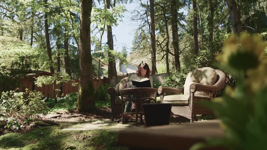 Woman sits outside on lawn furniture reading a book