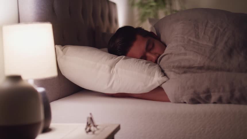A man fidgets while sleeping in a bed in brightly lit room