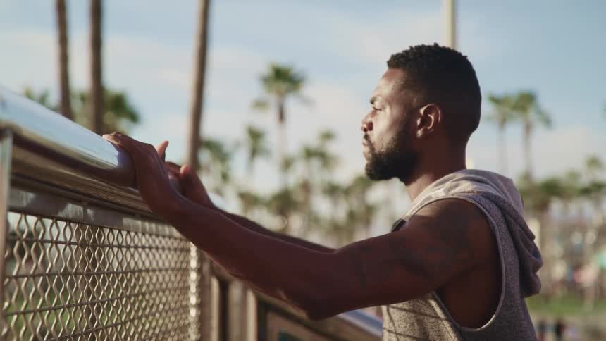 A young black man leans on a fence and looks over it