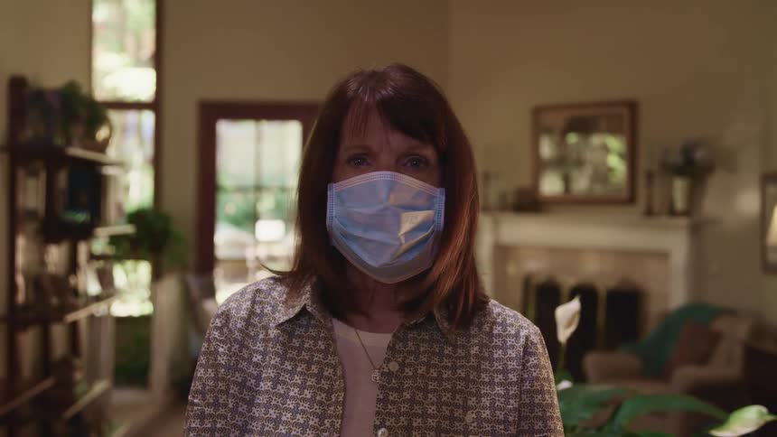 A woman in her home wearing a mask