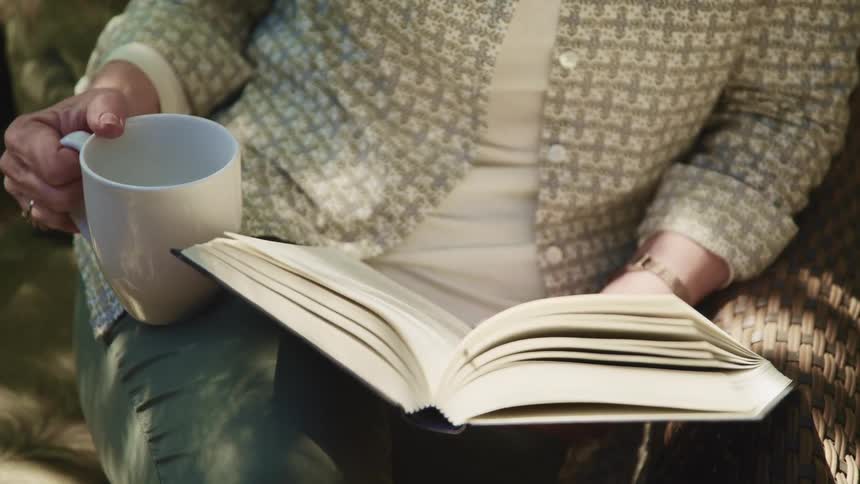 Woman sitting on a couch reading a book while drinking a hot beverage
