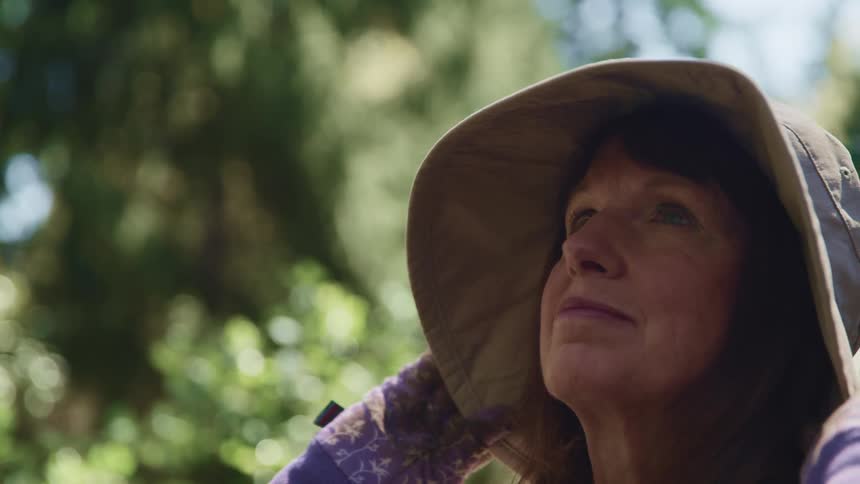 A woman with a hat and gloves standing with trees and the sky in the background