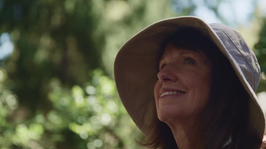 A woman in a hat smiling looking at trees