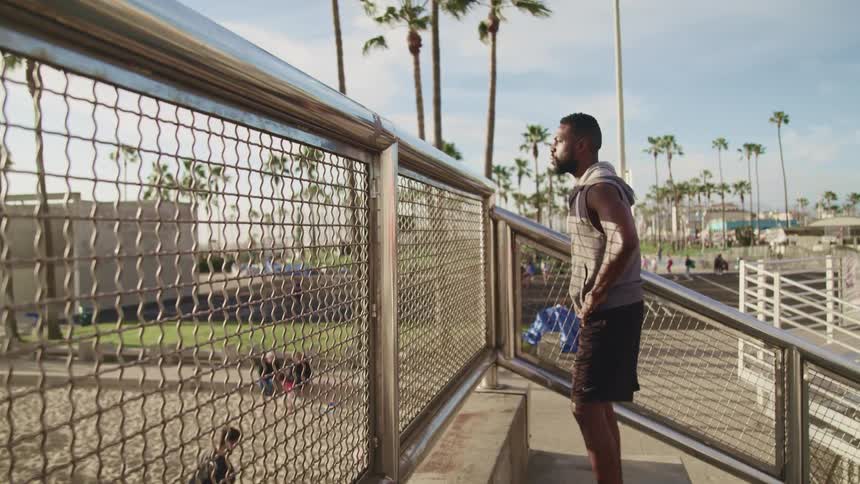A man stands at the top of some stairs and looks out at people walking in a public park