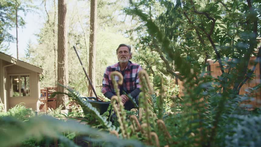 An elderly man sits outside his home in his garden