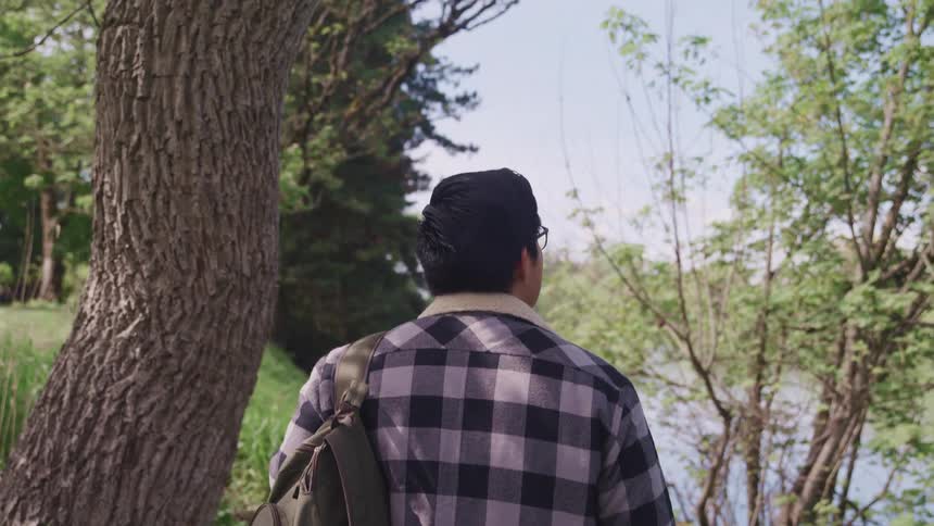 A young man walks past trees and towards a lake