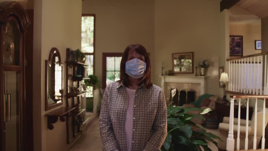 Woman wearing a face mask stands in the living room of a house