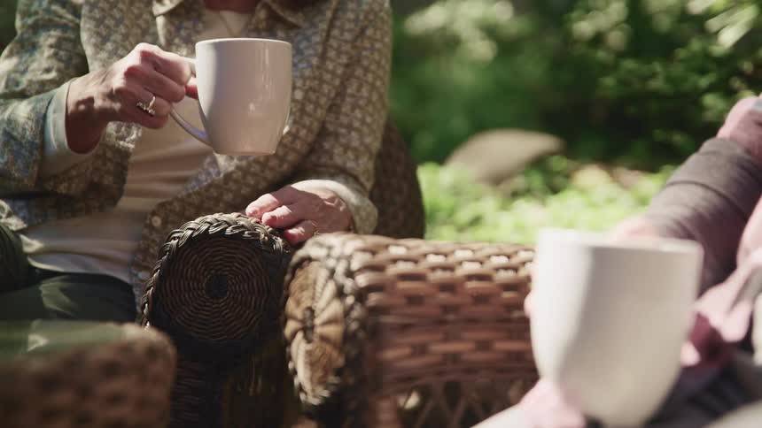 Middle aged man and woman sitting in armchairs drink coffee in the garden