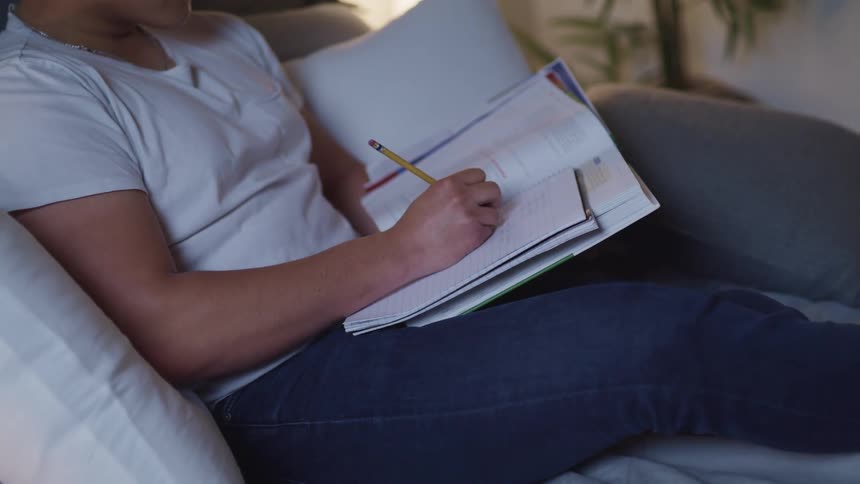 A woman sitting on a couch writing on a notebook with a pencil
