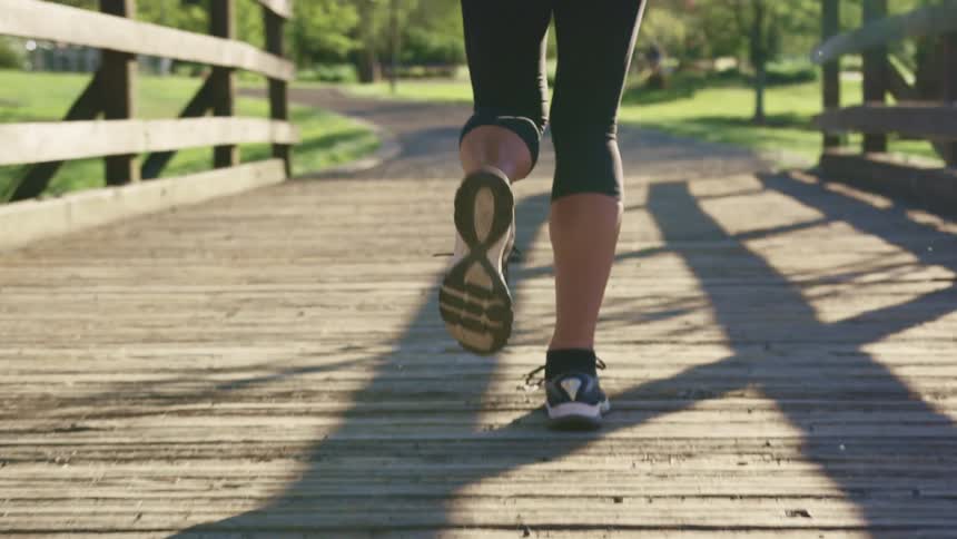 Woman with running shoes tights runs across a timber bridge on a sunny day