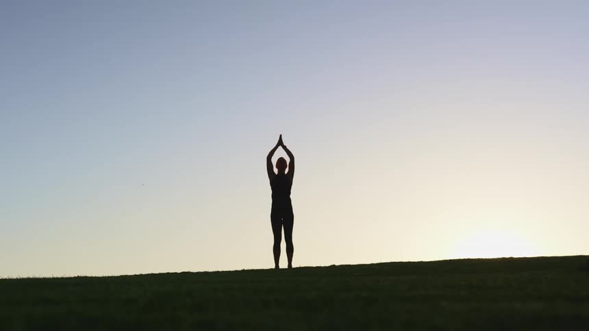 Silhouette of a woman doing yoga outdoors at sunset