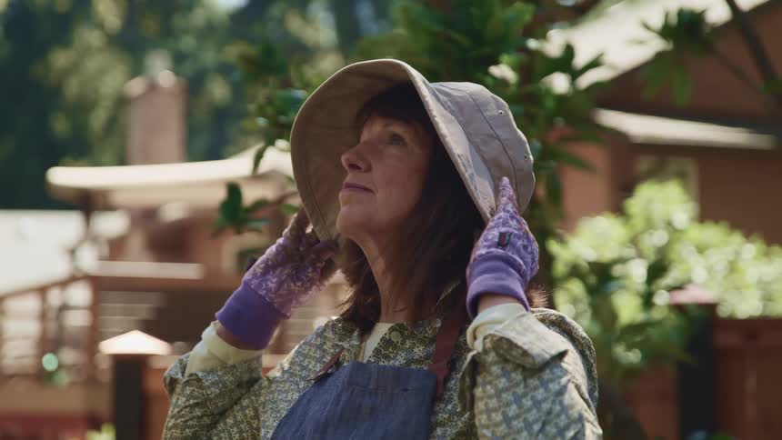 A woman adjusts her hat while gardening in her yard