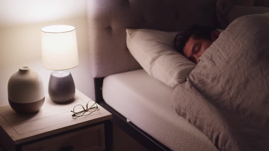 A man sleeping in a bed covered in a blanket next to a nightstand