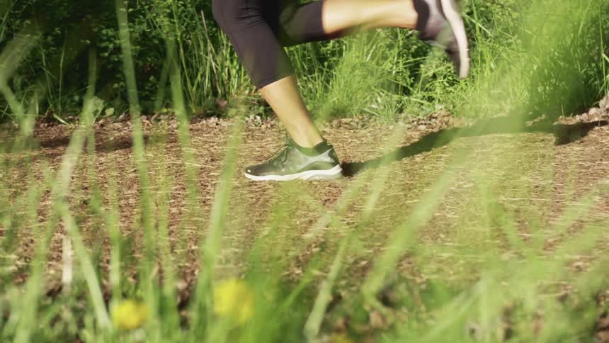 Woman with black tights and running shoes jogs along a dirt road