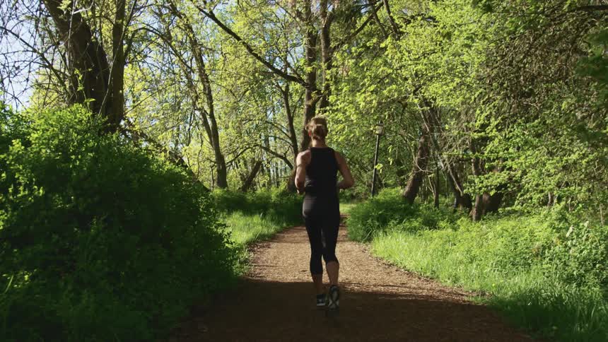 A woman in athletic gear jogs down a dirt path through a woodland