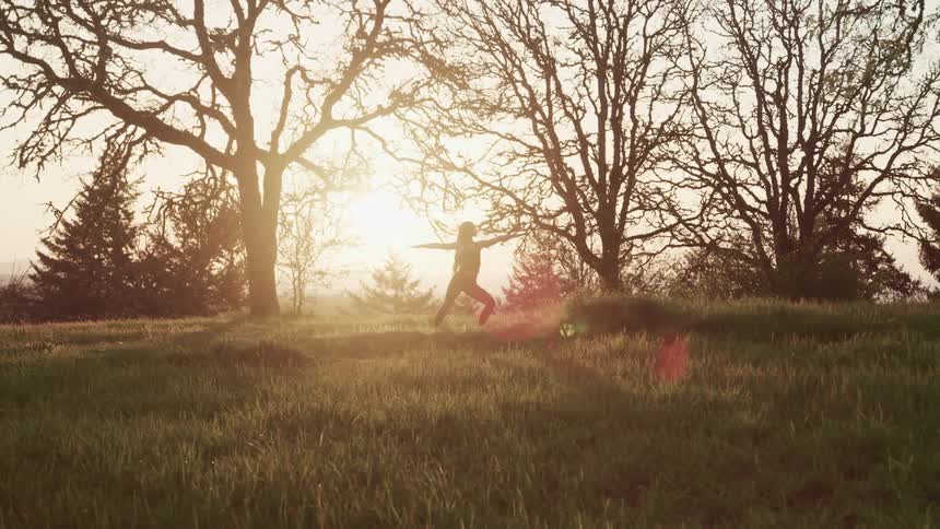 Young woman in sports clothing practices yoga in the grass at sunset