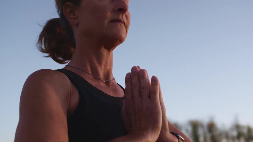 A woman meditates outdoors with her eyes closed and hands held together in a prayer position