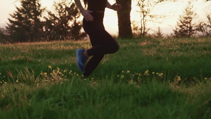 A woman in athletic wear jogs through a field at sunrise