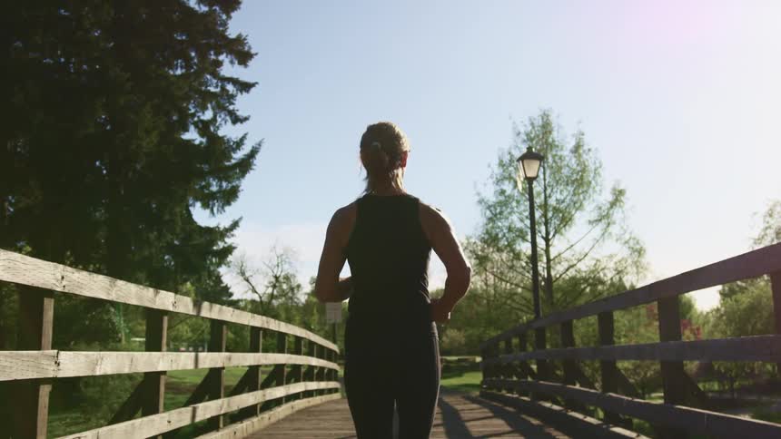 A woman in athletic wear jogs across a wooden bridge in a public park during the day