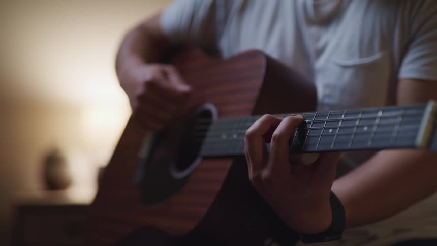 Man in white shirt plays acoustic guitar in a dimly lit room