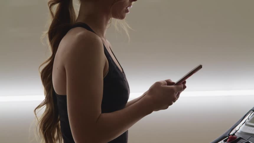 A teenage girl texts on her cell phone as she walks on a treadmill