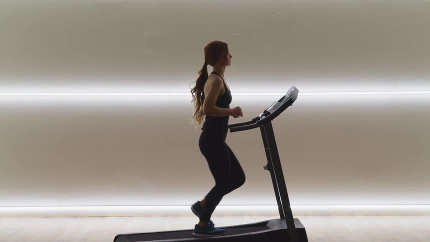 Woman wearing sports clothes runs on a machine in a gym