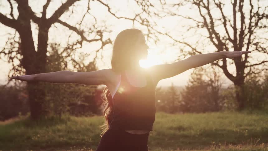 A woman stretching with grass trees and the sky in the background