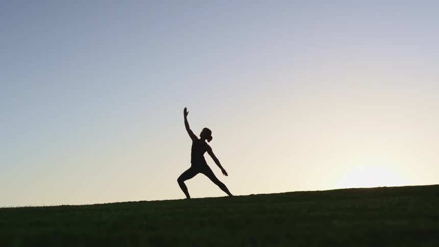 Woman performs yoga on top of hill silhouetted by light