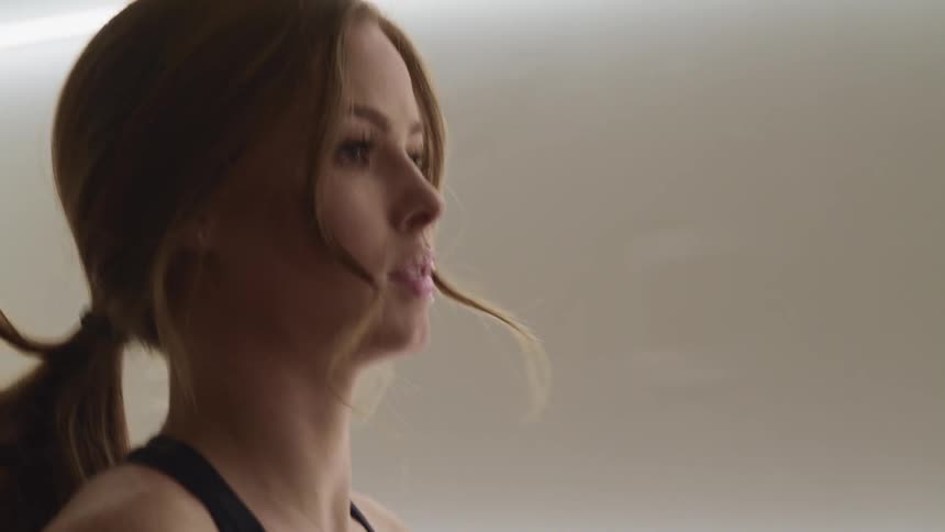 Woman with makeup and a brown ponytail runs a treadmill in a room