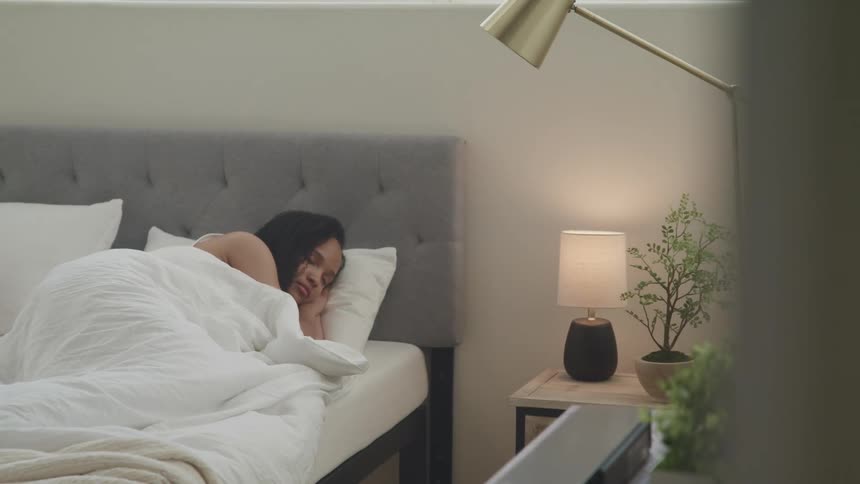 Woman with a sad expression lays in bed under the sheets in the bedroom
