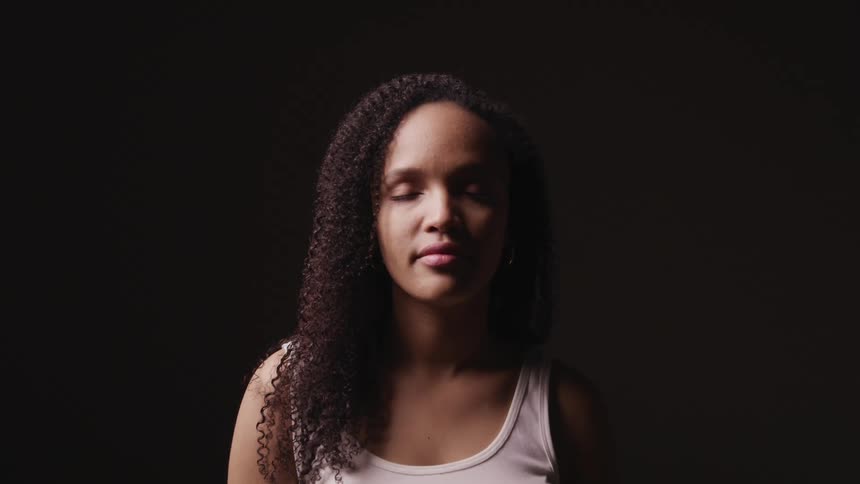 Black woman with curly hair faces the camera with eye contact on a dark background
