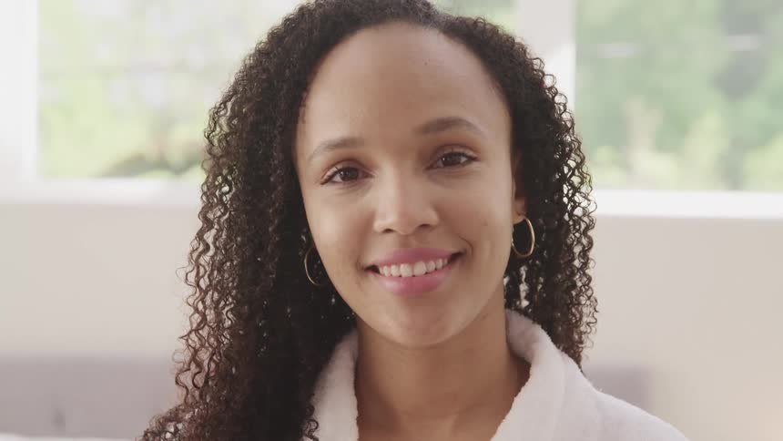 A young woman in a white bath robe turns her head to smile into the camera