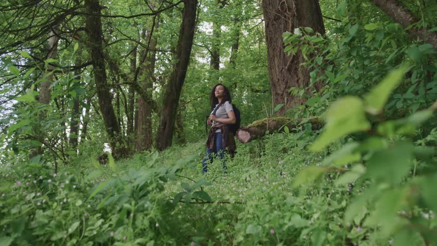 A woman stands in the forest with her eyes closed