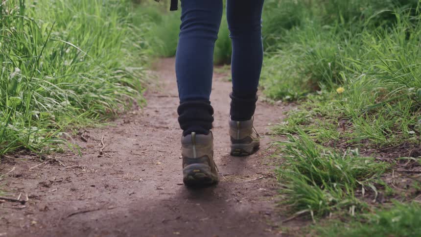 Woman wearing boots and jeans walks along a forest track